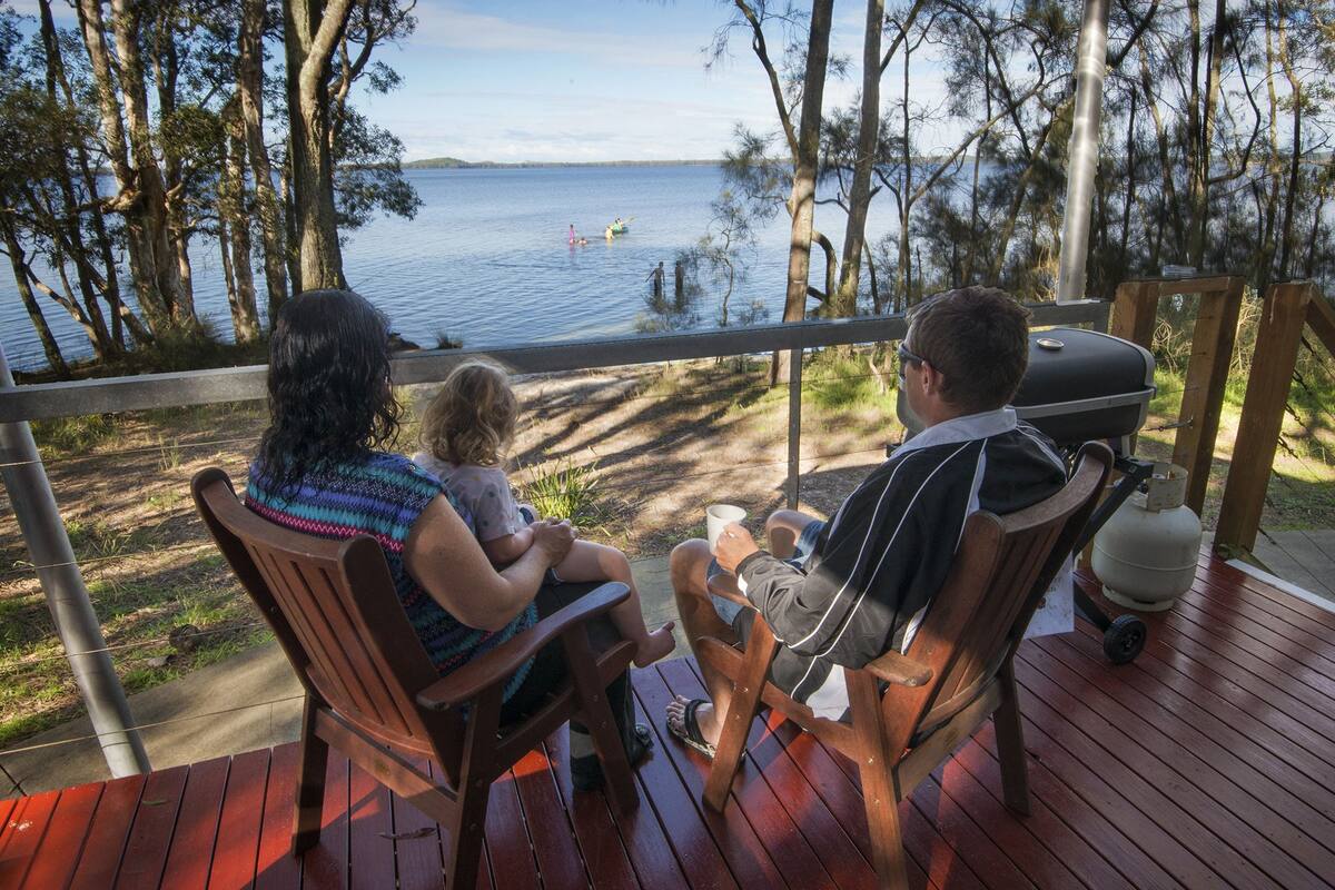 Une terrasse en bois donnant sur un lac, avec un barbecue et un espace salon.