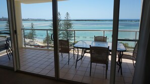 A balcony with a table and chairs, overlooking a coastal view with turquoise water and distant land. - Moorings Beach Resort (Golden Beach)