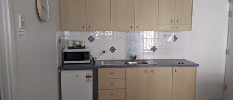 Una cocina compacta con armarios de madera, microondas, refrigerador pequeño y pileta.