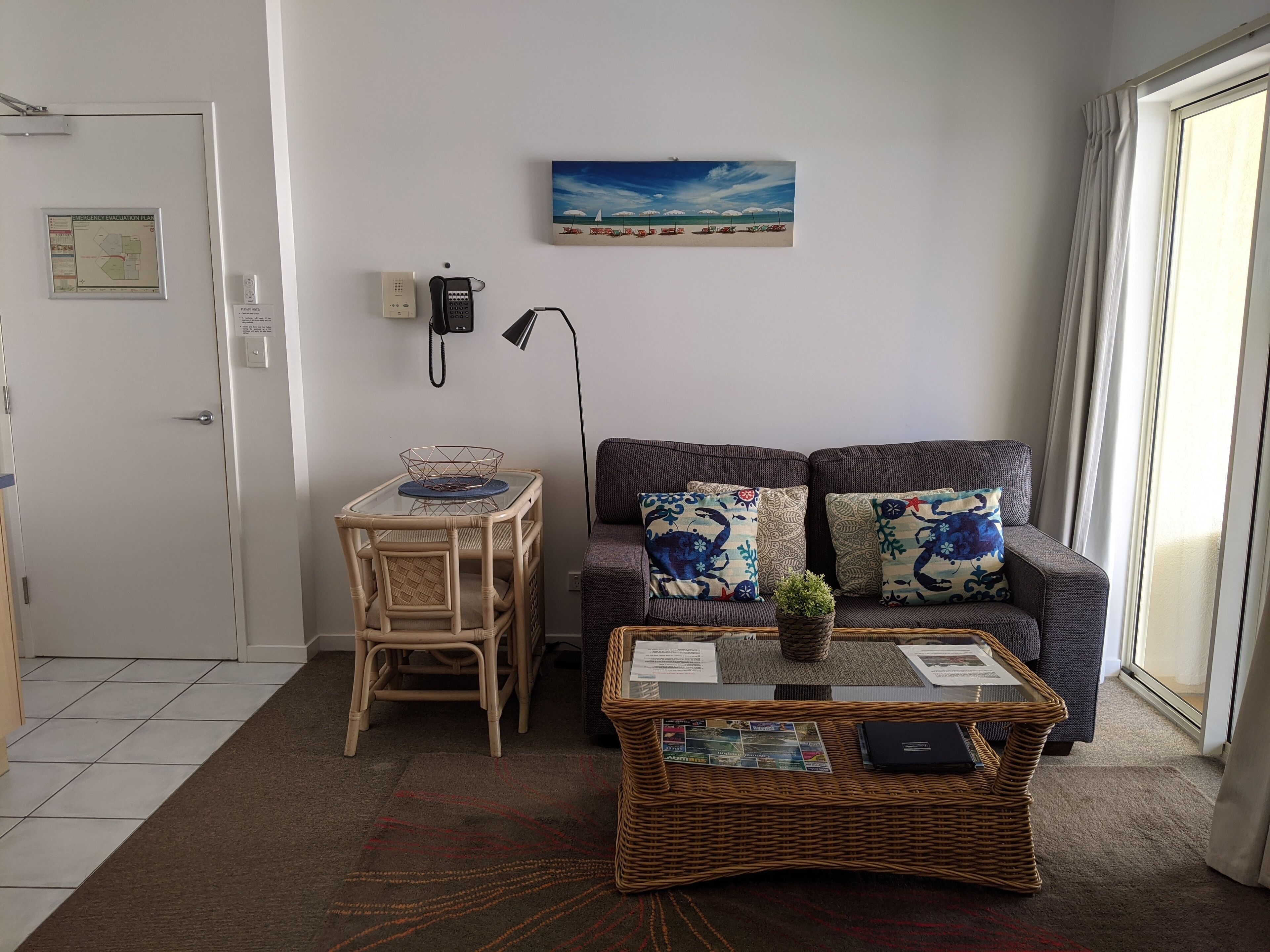 A living room with a sofa, a small table with a basket, a wicker coffee table, and a painting on the wall.
