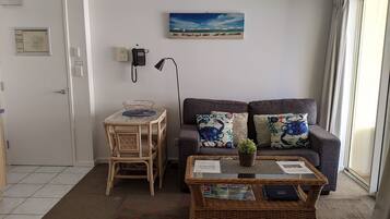 A living room with a sofa, a small table with a basket, a wicker coffee table, and a painting on the wall.
