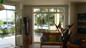 A reception area with a bench, a large window, and a plant. - Moorings Beach Resort (Golden Beach)