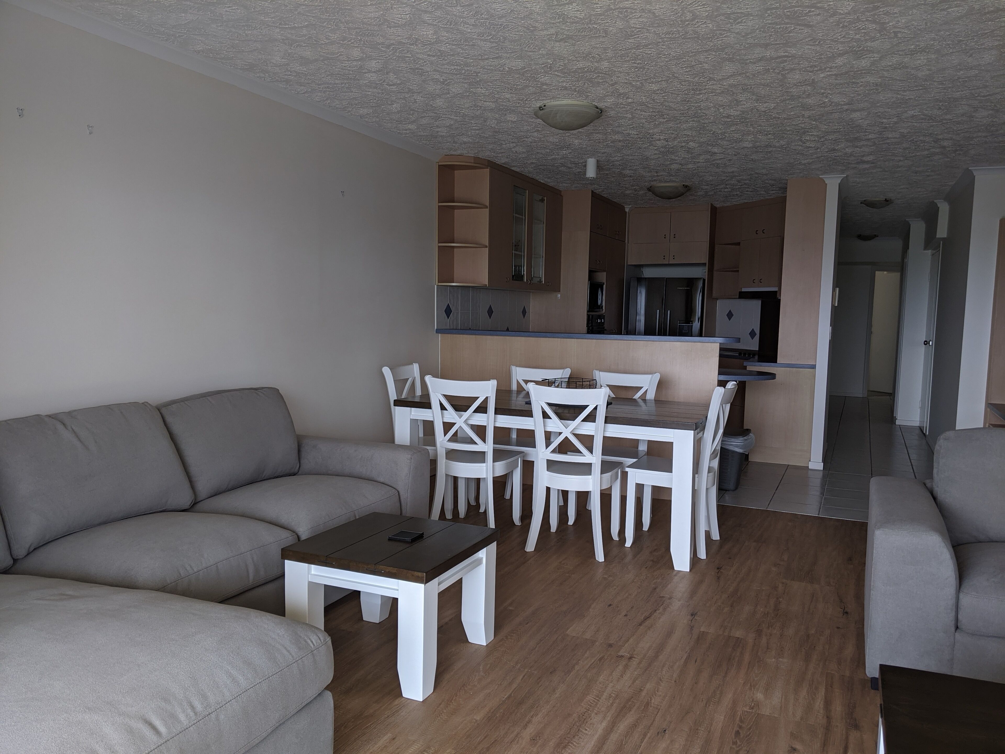 A modern living room with a grey sofa, a small white table, and a dining area with white chairs.