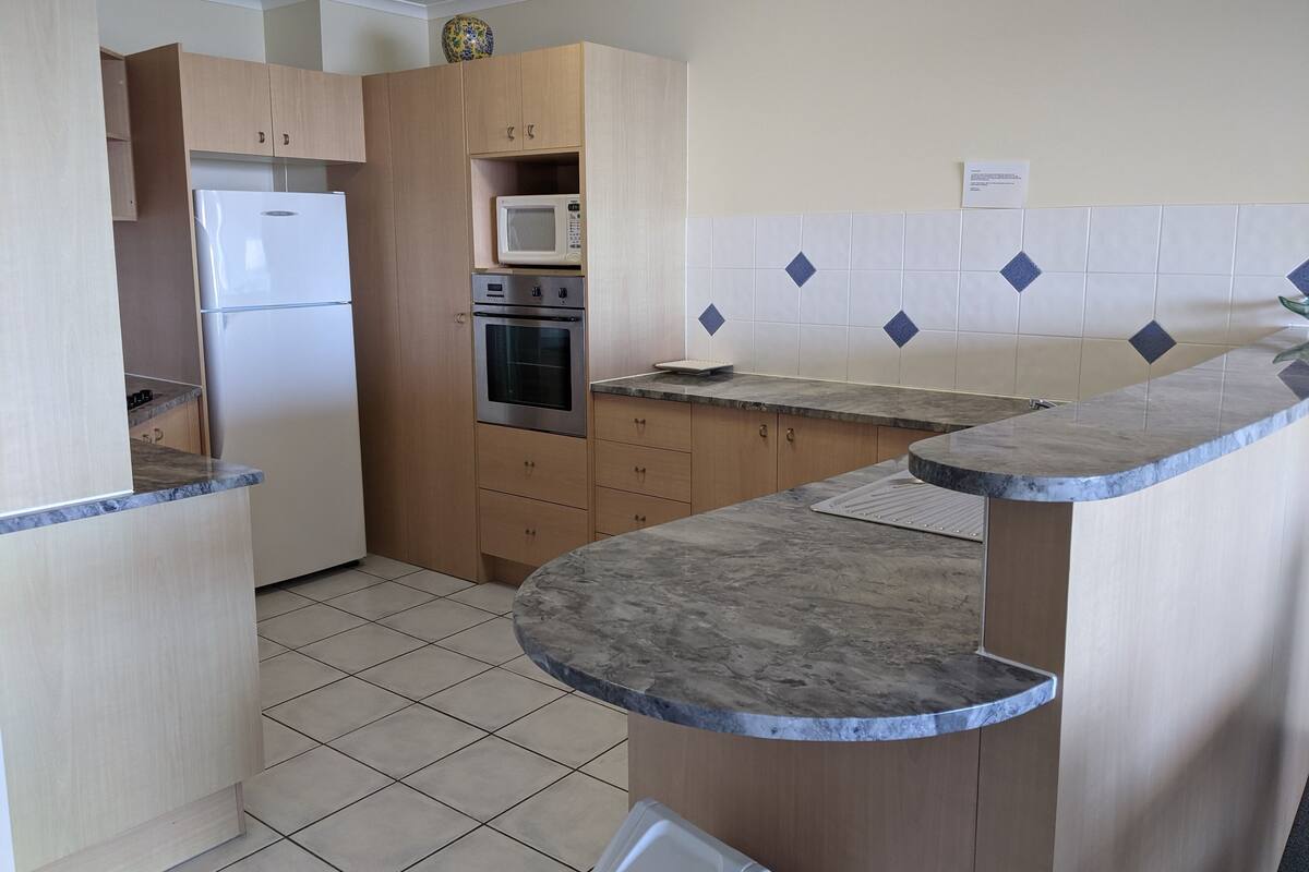 Una cocina con armarios de madera, horno empotrado, microondas y encimera de mármol.