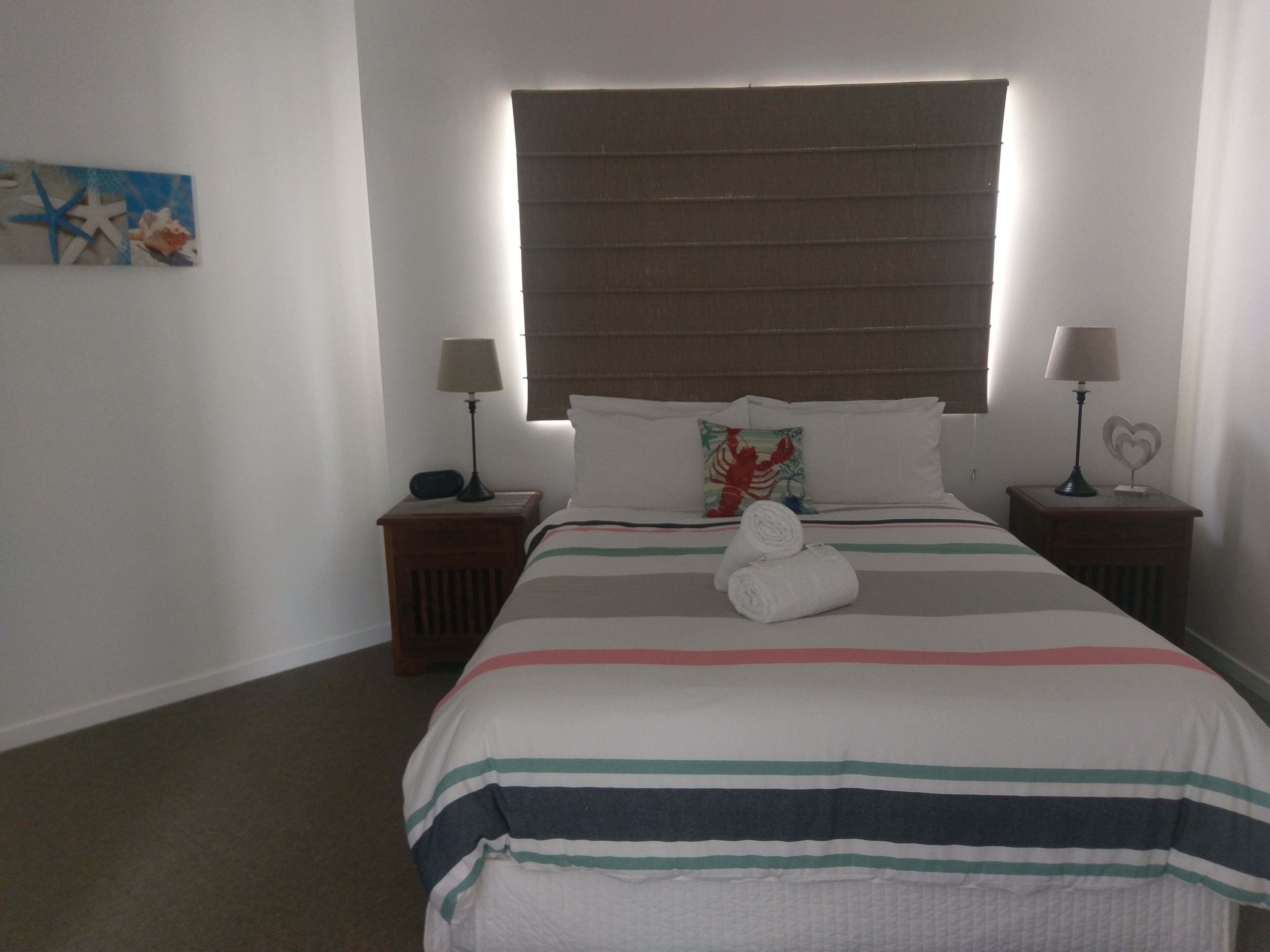 A hotel room with a large bed, two bedside tables with lamps, a headboard, and a wall decoration.