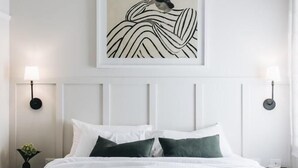 A neatly arranged bedroom with a bed, two bedside tables, a wall-mounted artwork, and two wall sconces. - The Dormie House - On The Golf Course (Moss Vale)