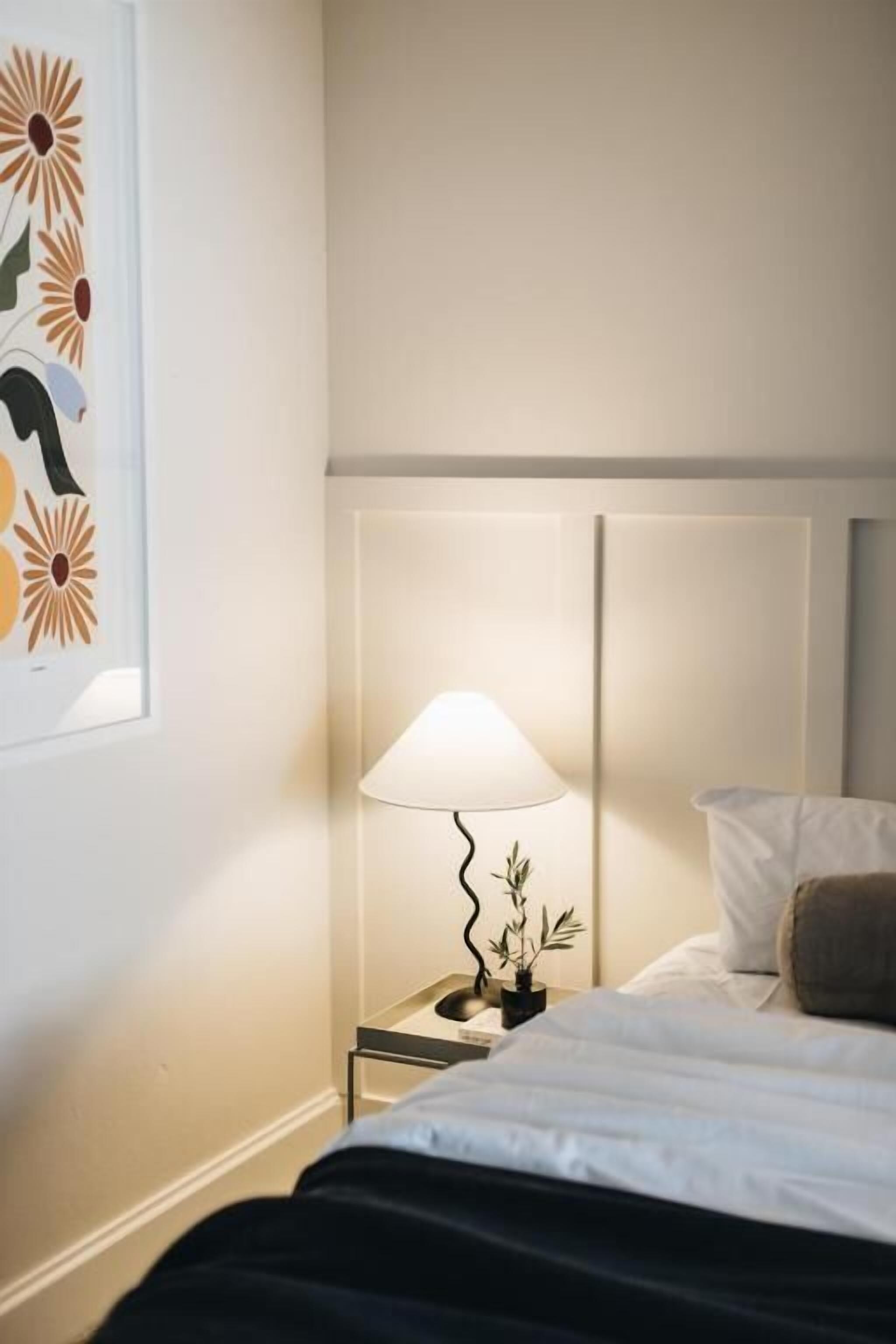 Une chambre d’hôtel avec un lit, une table de chevet avec une lampe et une œuvre d’art encadrée au mur.