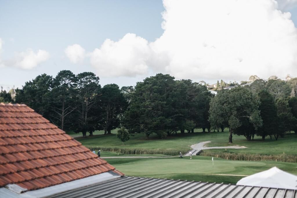 A golf course with a clear sky, trees, and a building with a red roof.
