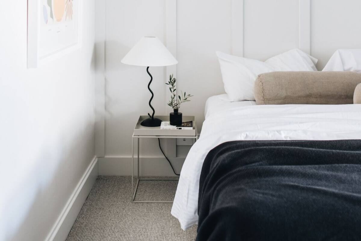 A hotel room with a bed, a nightstand with a lamp, and a framed floral artwork on the wall.
