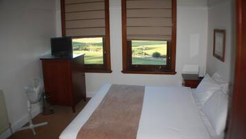A bedroom with a bed, a television on a wooden cabinet, and two windows with a view of a golf course.