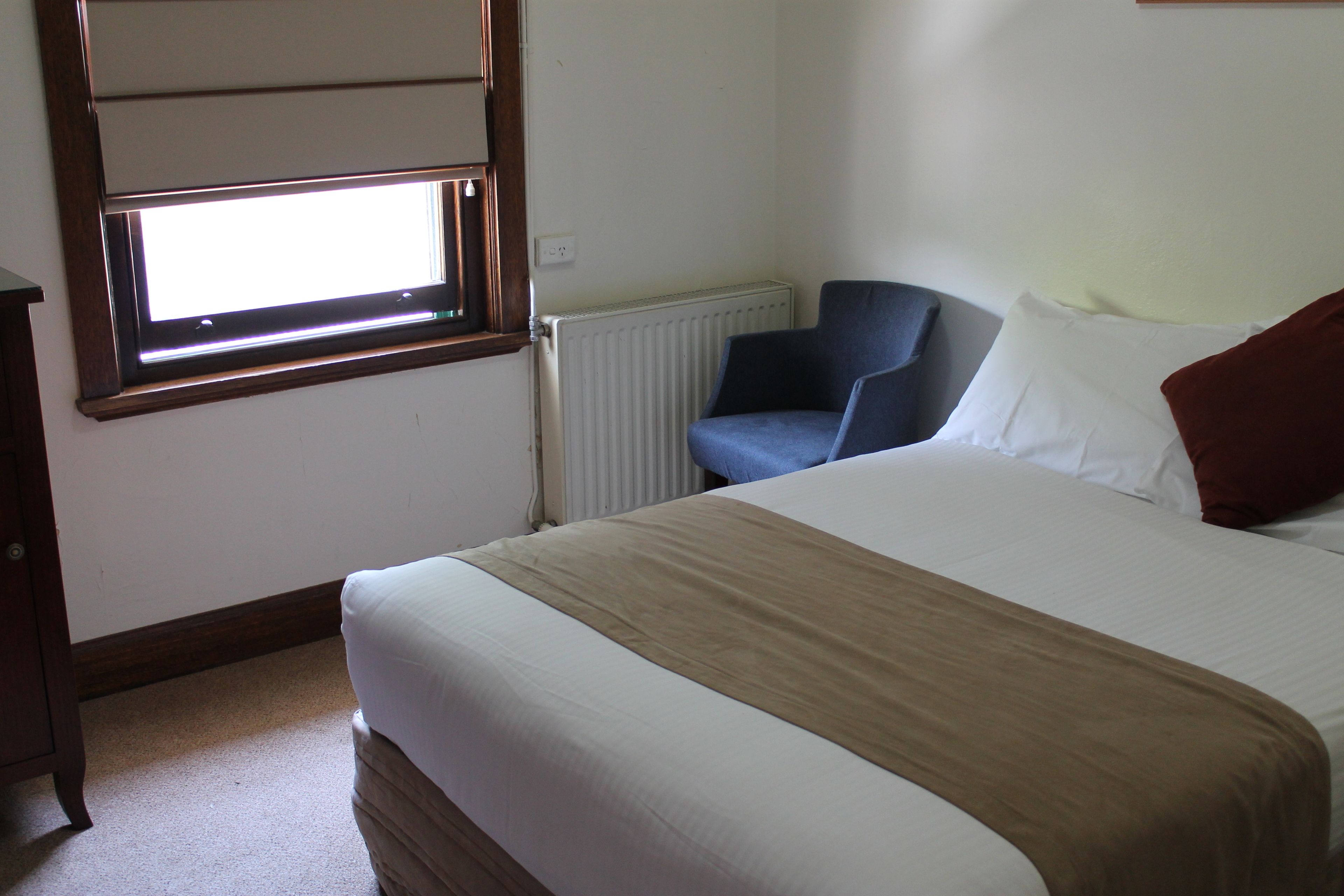 A bedroom with a bed, a window, a radiator, and a chair.