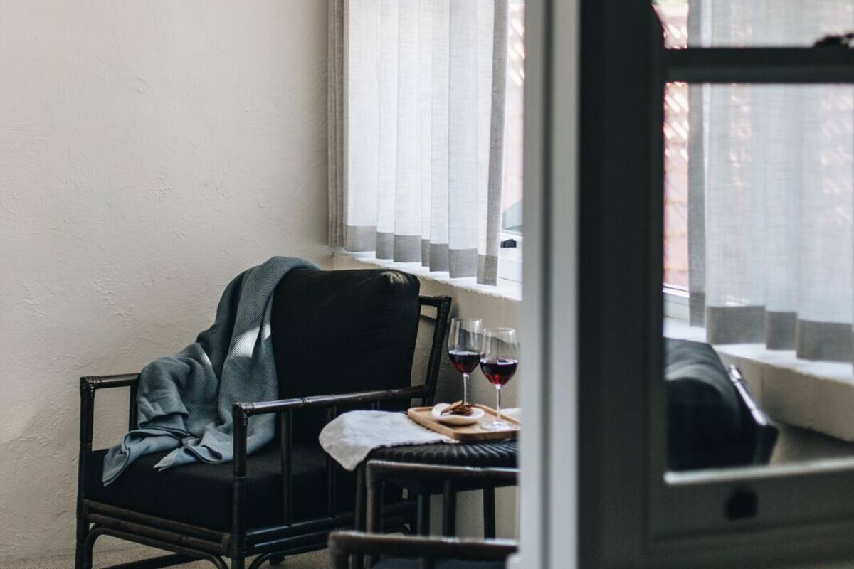 A room with a black chair, a small table with a tray, and a window with sheer curtains.