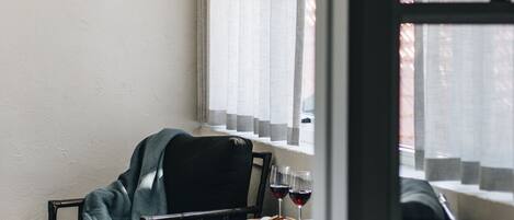 Una habitación con una silla negra, una mesita con una bandeja y una ventana con cortinas de gasa.