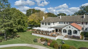 A large, two-story building with a patio area featuring outdoor seating and umbrellas. - The Dormie House - On The Golf Course (Moss Vale)