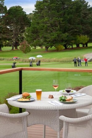 A dining table with food and drinks, overlooking a golf course. - The Dormie House - On The Golf Course (Moss Vale)