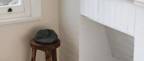 A corner of a room with a white fireplace, a small stool with a hat, and a black bag on the floor.