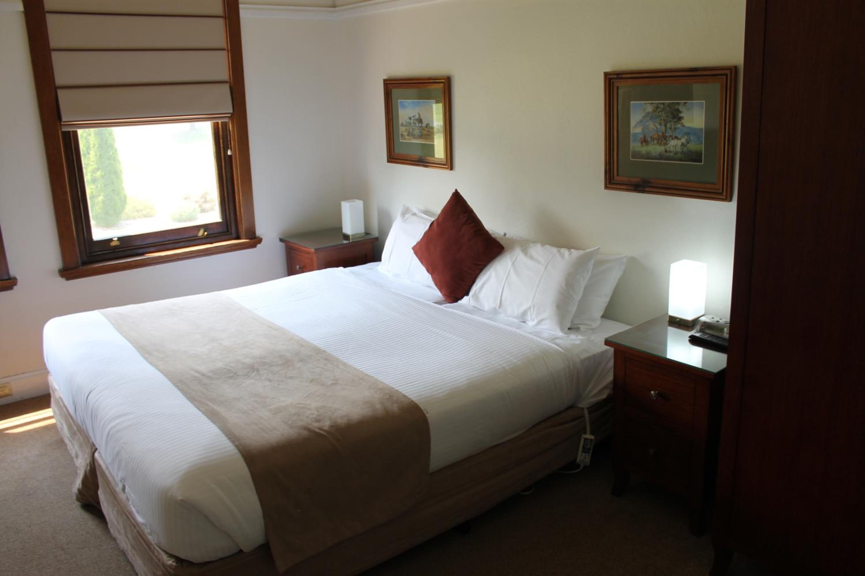 A neatly made bed with a brown accent pillow, a bedside table with a lamp, and two framed pictures on the wall.