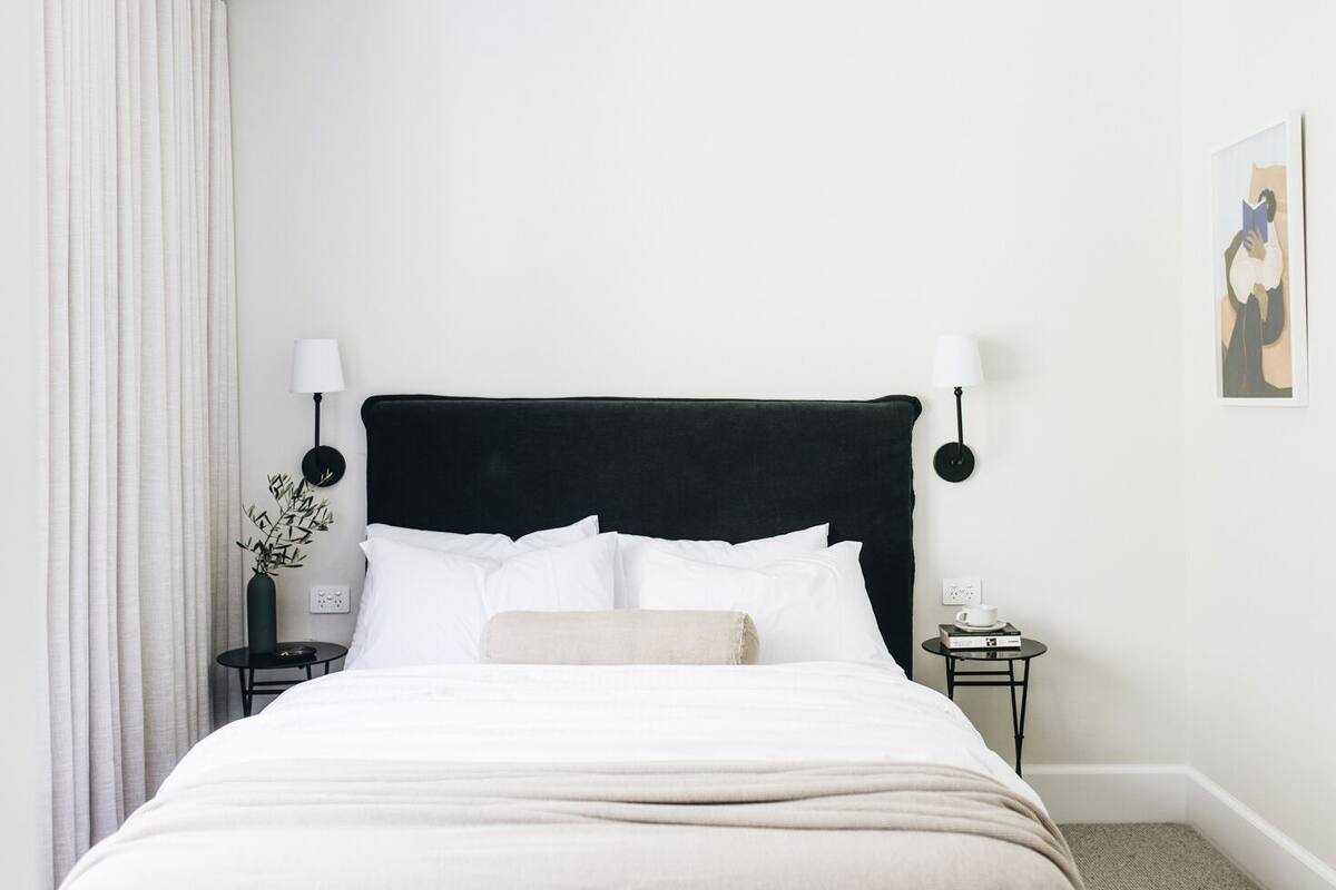 A neatly made bed with white linens, a black upholstered headboard, and two bedside tables with lamps.