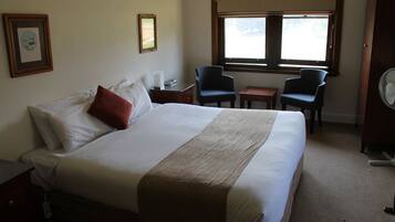 Una habitación de hotel con una cama grande, dos sillas, una mesita y un ventilador.