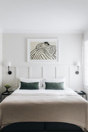 A neatly made bed with a white headboard and two green pillows, a framed artwork above the bed, and a bedside table with a lamp. - The Dormie House - On The Golf Course (Moss Vale)
