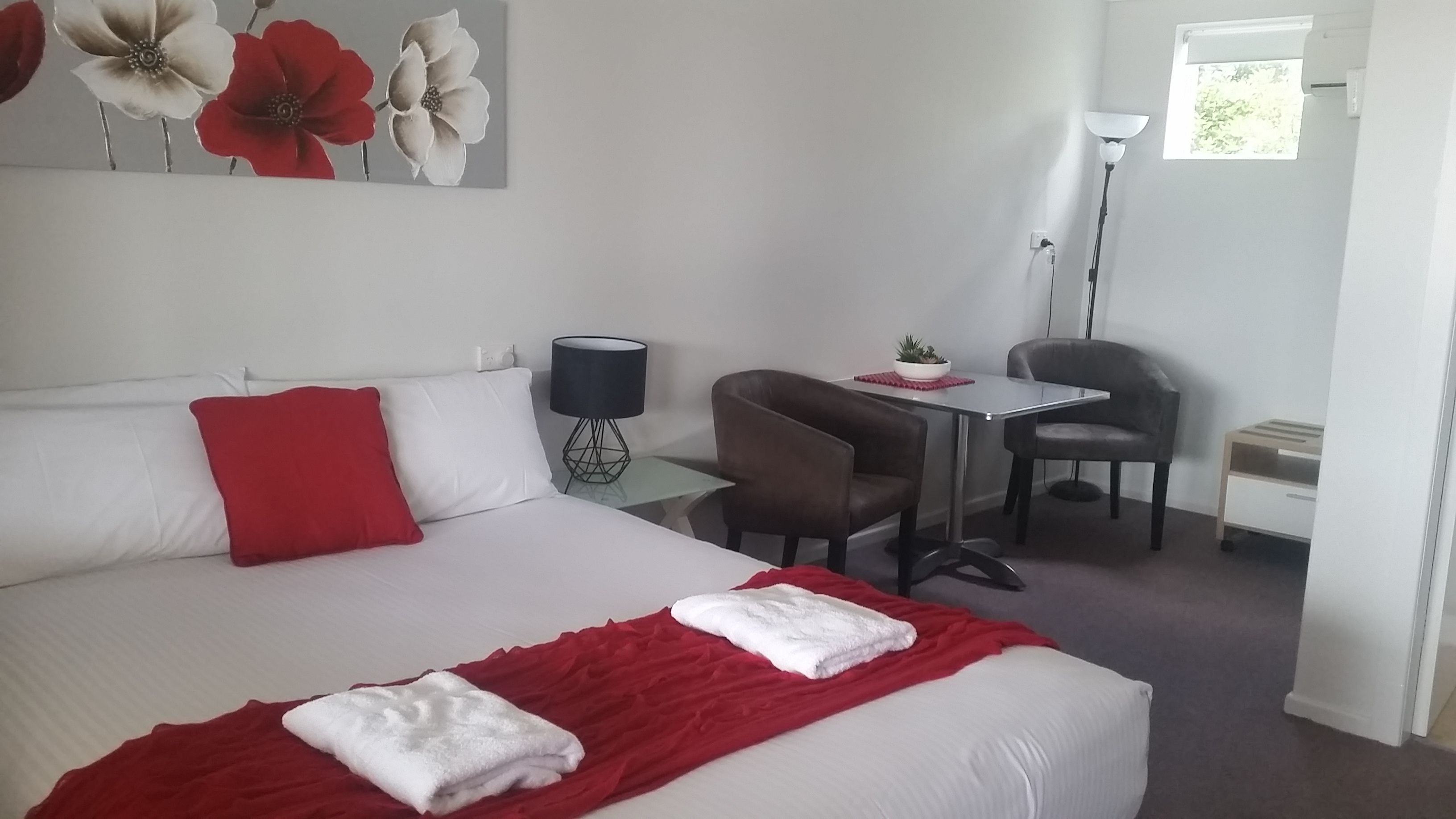 Una habitación de hotel con cama, escritorio, silla, lámpara y ventana.