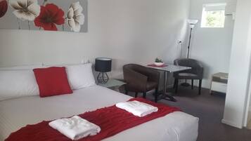 Una habitación de hotel con cama, escritorio, silla, lámpara y ventana.