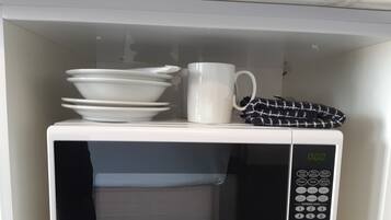Un forno a microonde bianco con display digitale, piatti bianchi impilati, una tazza bianca e un tovagliolo a quadri bianchi e neri.