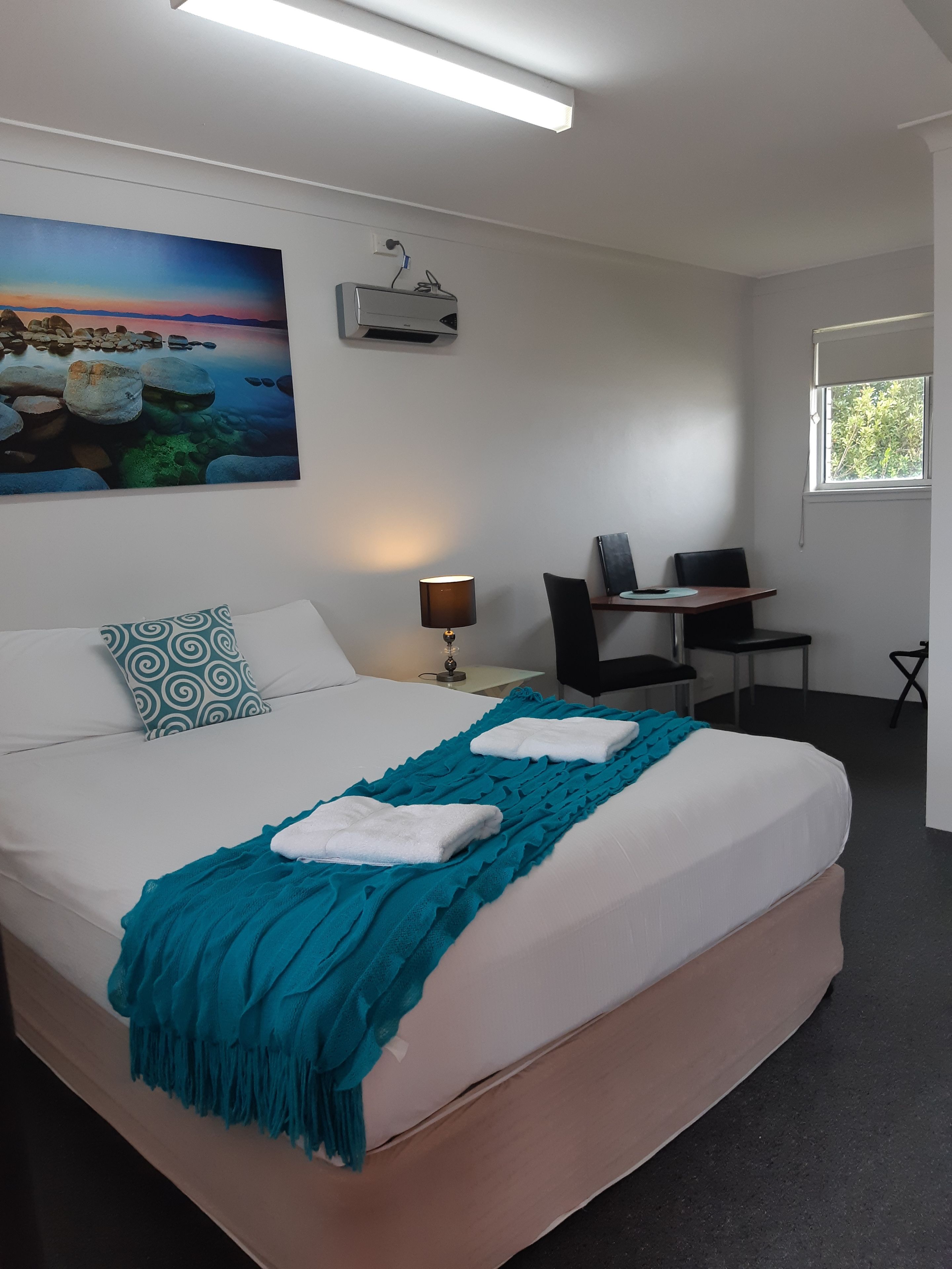 Una habitació d'hotel amb un llit gran, una escriptori, una cadira, un ordinador i un quadre a la paret.