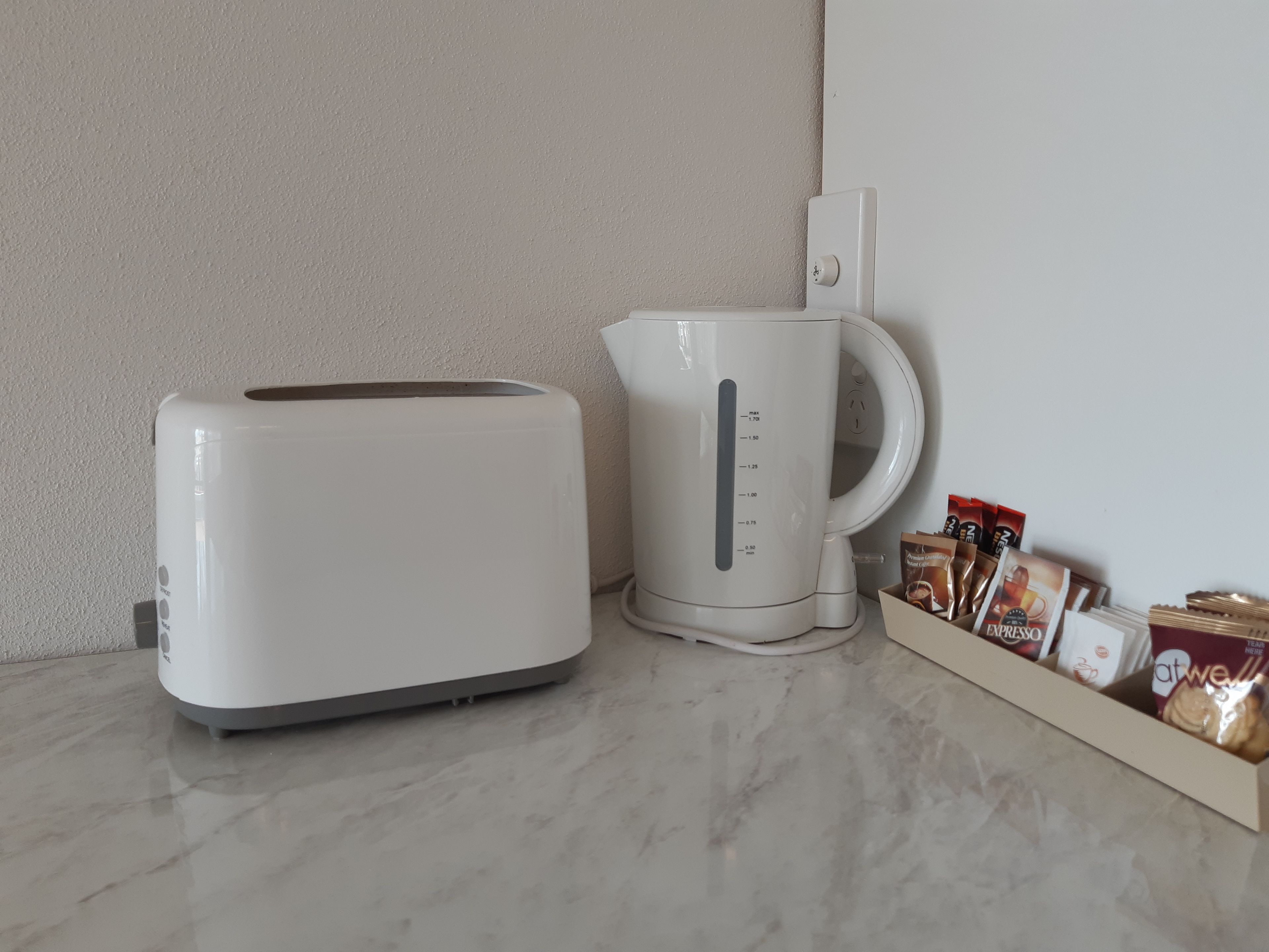 Una cocina con un tostador blanco, una cafetera blanca y un dispensador de cápsulas de café con varias marcas.
