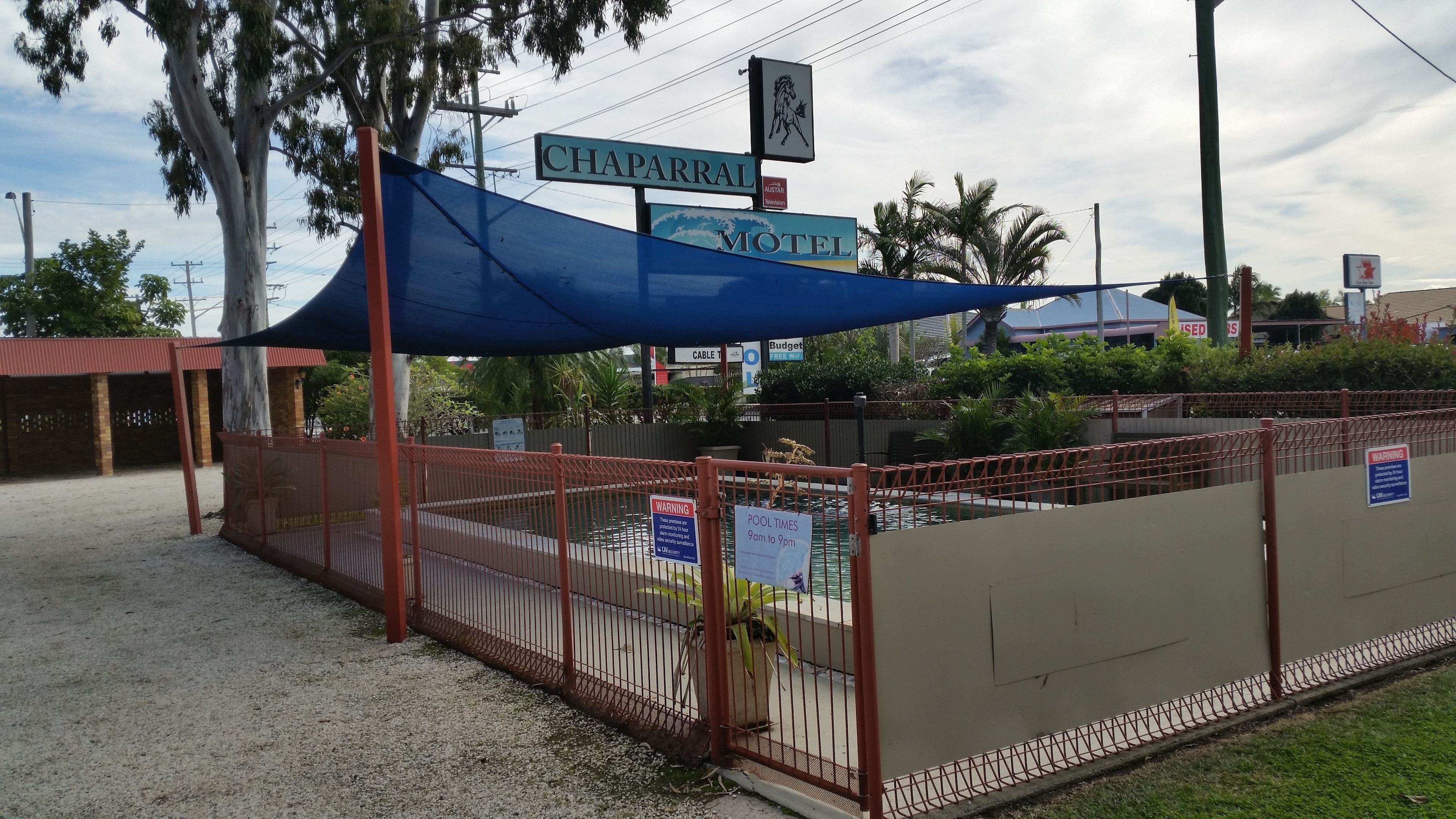 Un motel con un letrero que indica que es el Chapparral Motel, que cuenta con un área de piscina y horarios exhibidos.