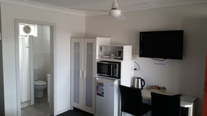 A compact kitchenette with a refrigerator, microwave, and coffee maker, a small table with chairs, and a TV mounted on the wall. - Econo Lodge Chaparral Motel Ballina (West Ballina)