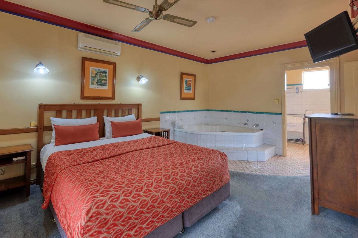 A hotel room with a bed, a large window, a ceiling fan, and a bathtub.