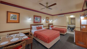 A hotel room with two beds, a dining table with chairs, and a bathroom with a sink and mirror.
