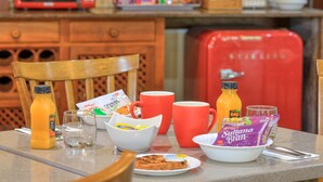 A breakfast table with orange juice, a bowl of cereal, a plate of toast, and a red mug.