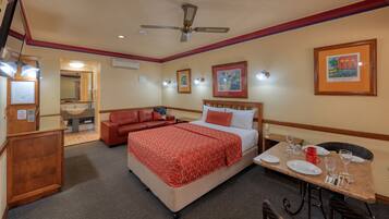 A hotel room with a bed, a sofa, a dining table with plates and glasses, a ceiling fan, and framed artwork on the walls.