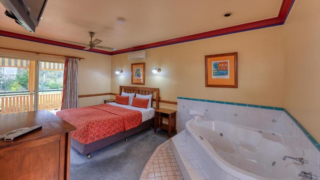 Habitación de hotel con cama, escritorio, televisión, ventilador de techo, ventana con cortinas y bañera.