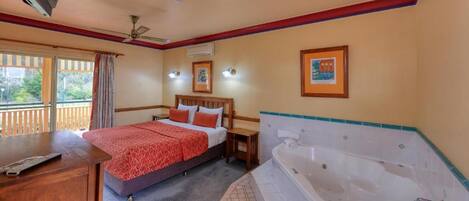 Habitación de hotel con cama, escritorio, televisión, ventilador de techo, ventana con cortinas y bañera.