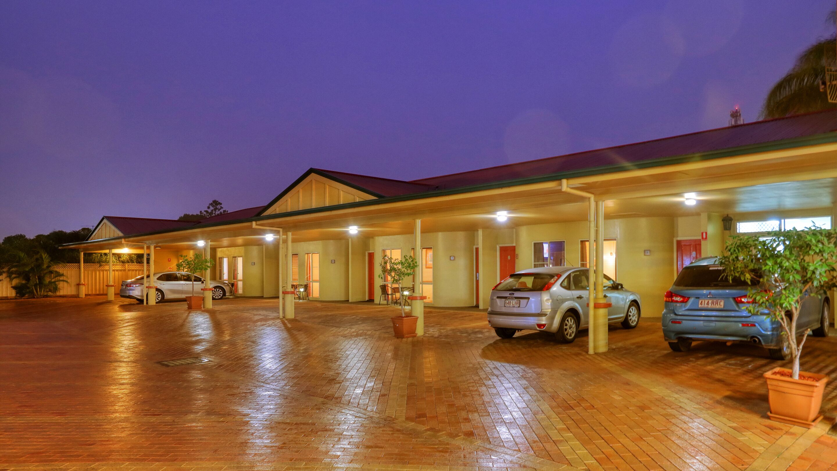 Un hotel con estacionamiento techado, varias habitaciones y piso de ladrillo.