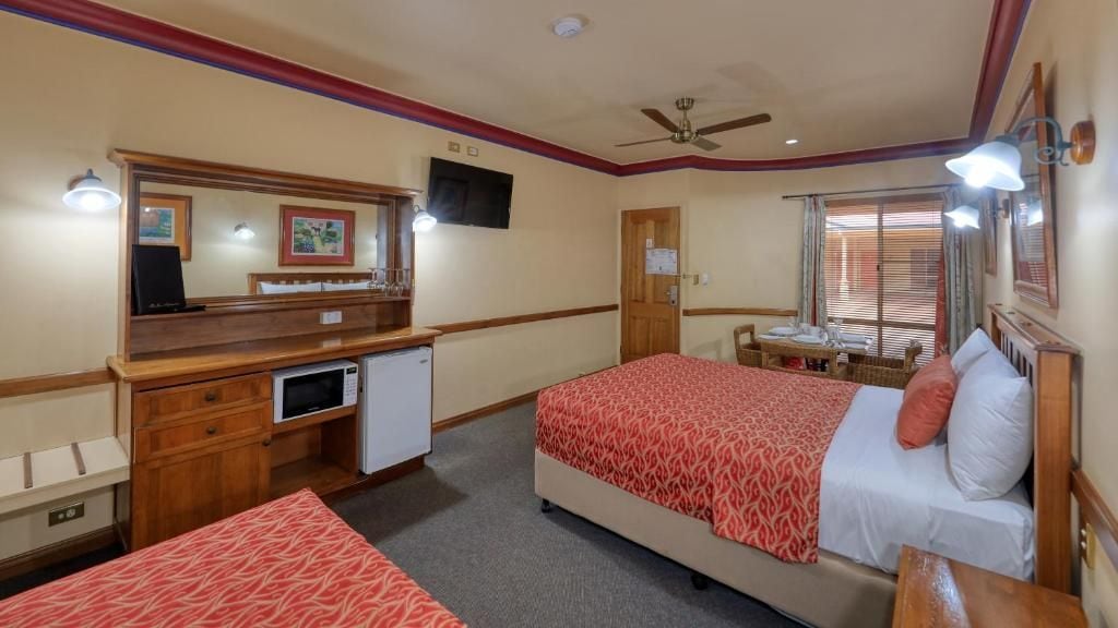 Una camera d'hotel con un letto, una scrivania, un forno a microonde, una televisione e una finestra con persiane.