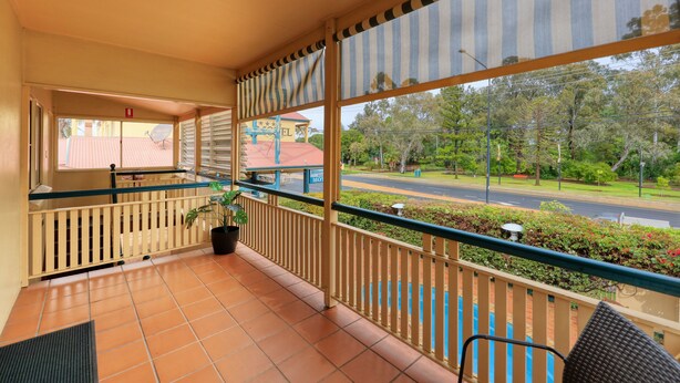 A balcony with a view of a street and greenery, a potted plant, and a chair.