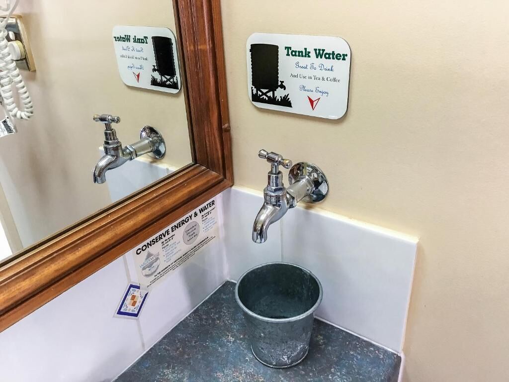 Un baño con un cartel que anima a usar el agua del tanque para beber, y en té y café, y un cartel que promueve el ahorro de energía y agua.