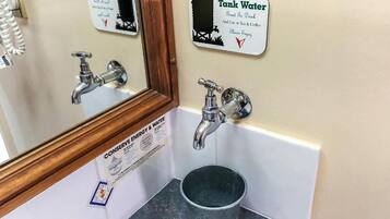 Un baño con un cartel que anima a usar el agua del tanque para beber, y en té y café, y un cartel que promueve el ahorro de energía y agua.