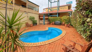 A motel with a swimming pool, outdoor seating, and a fenced patio area.