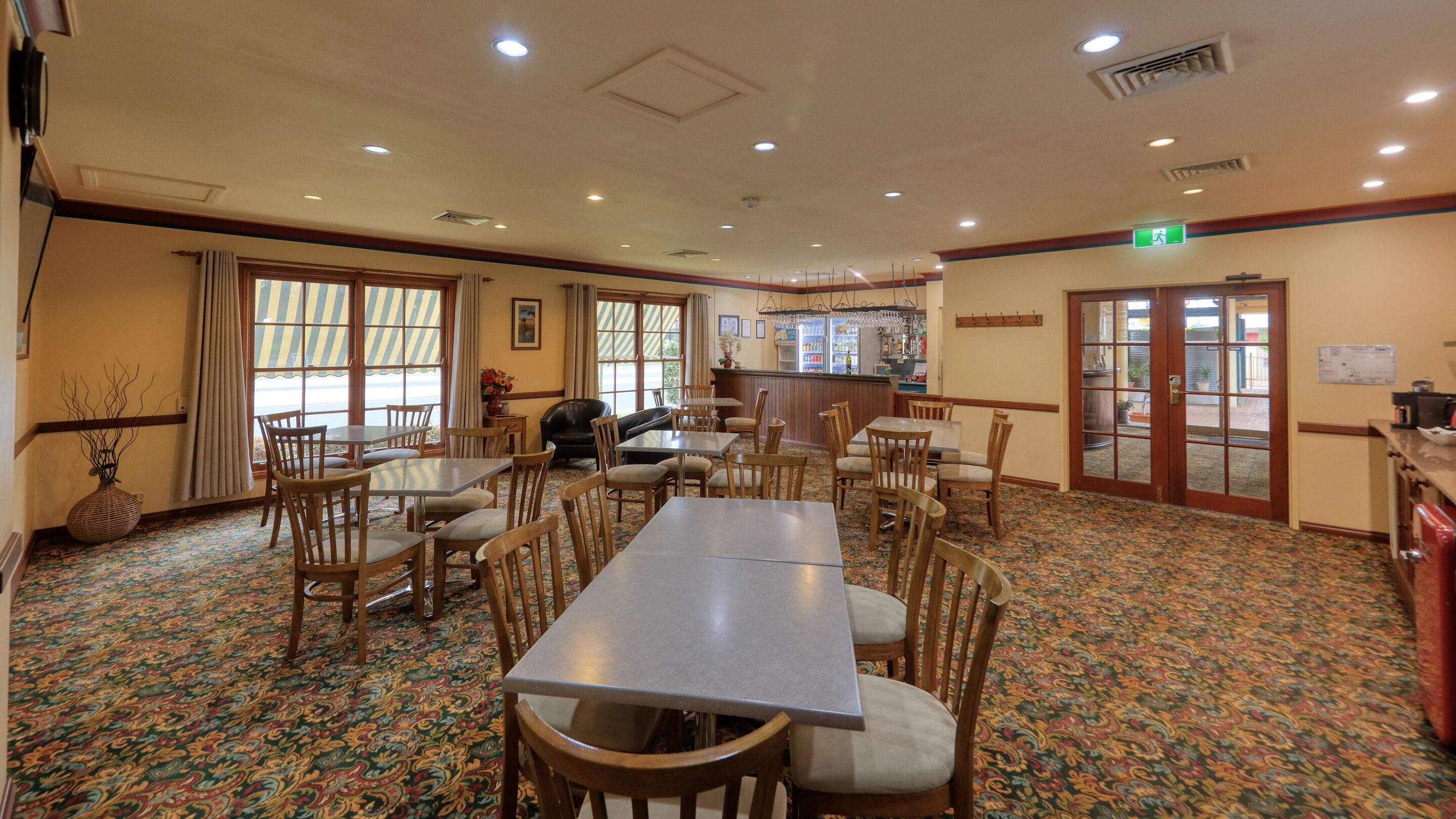 Un espace repas avec plusieurs tables et chaises, un bar et une vue dégagée grâce à de grandes fenêtres.