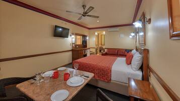 Una habitación de hotel con una cama, un televisor, un escritorio con una silla y una mesa de comedor para dos personas.