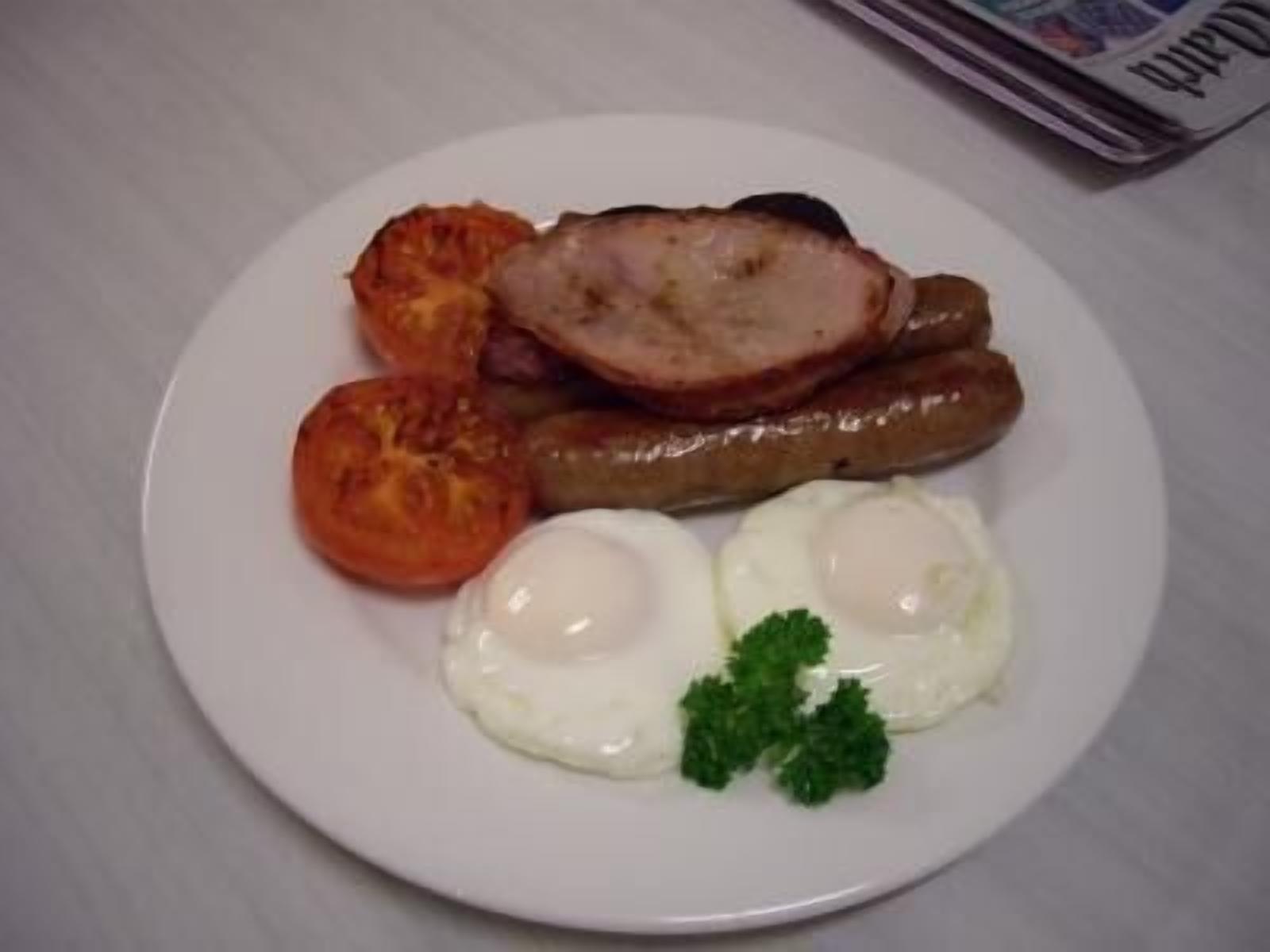 Un plato con huevos, salchichas, tomates y perejil.