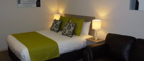 Habitación de hotel con una cama, dos lámparas de noche, un sofá de cuero negro y una obra de arte abstracta colgada en la pared.