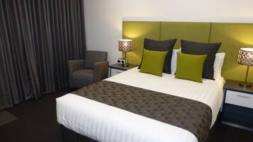 Una habitación de hotel con una cama grande, dos mesitas de noche con lámparas, una silla y una cortina.