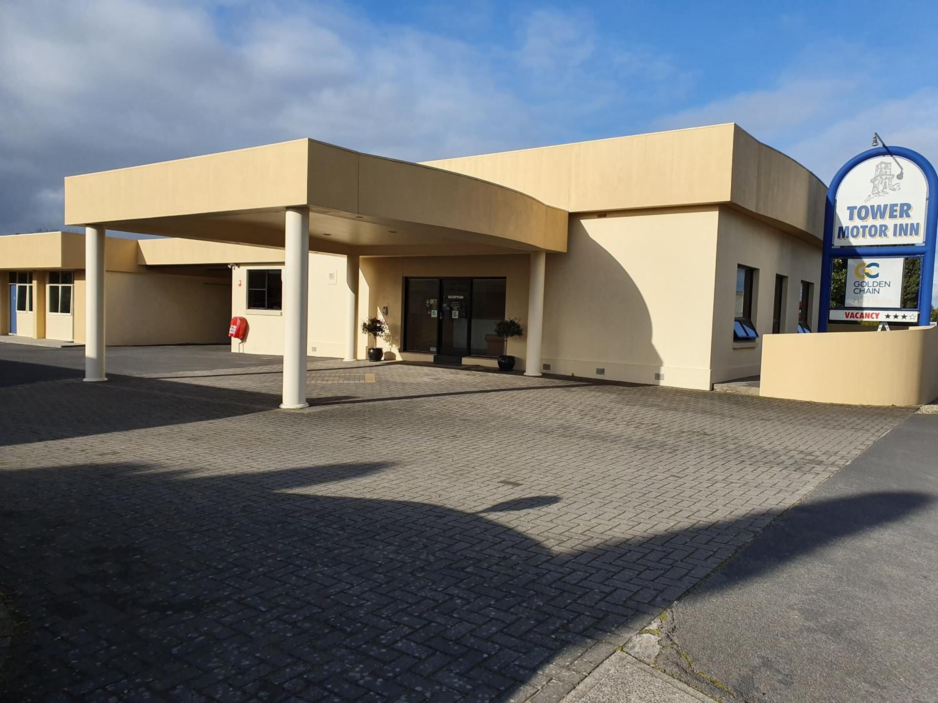 Een modern gebouw met een bord voor Tower Motor Inn, met een overdekte ingang en een zichtbare receptie.