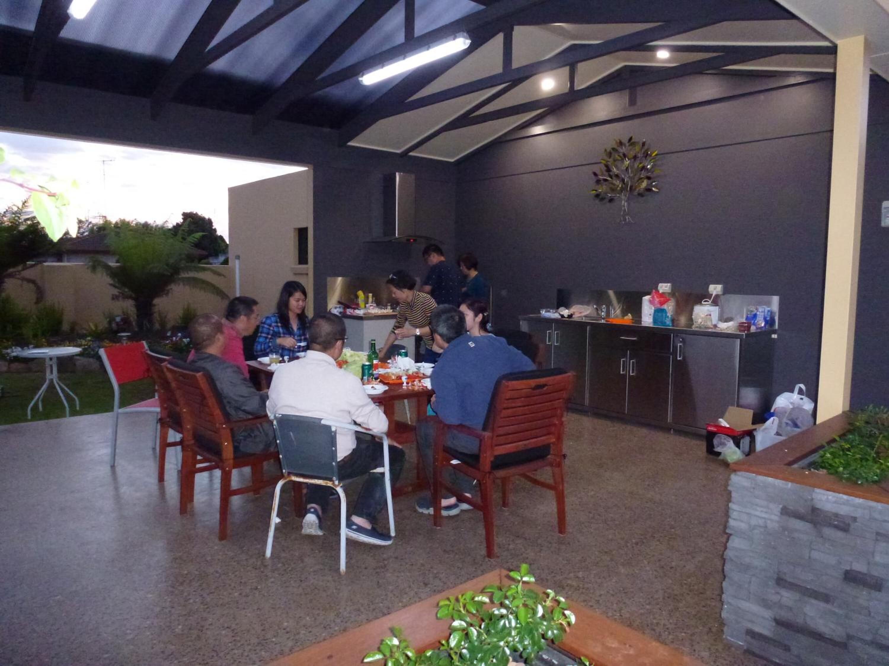 An outdoor dining area with a group of people seated at tables, a bar area, and a kitchen counter.